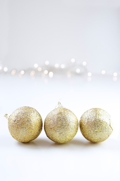 Trois boules de Noël dorées et quelques lumières sur fond blanc. Espace de copie.