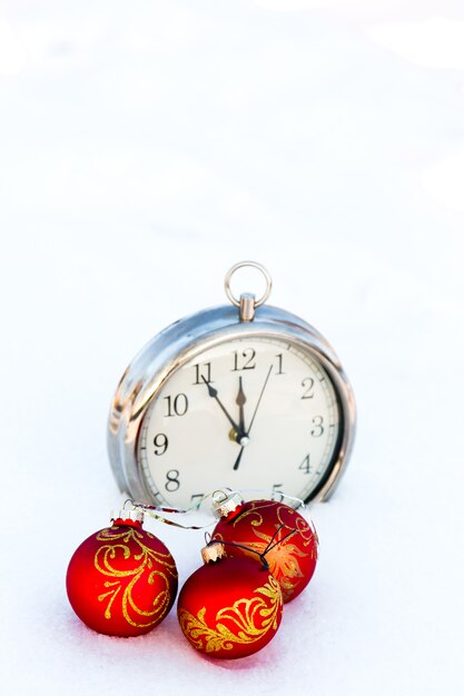 Trois boules de Noël rouges et horloge sur la neige