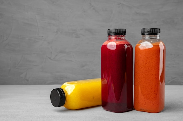 Trois bouteilles en plastique avec du jus fraîchement pressé sur fond gris