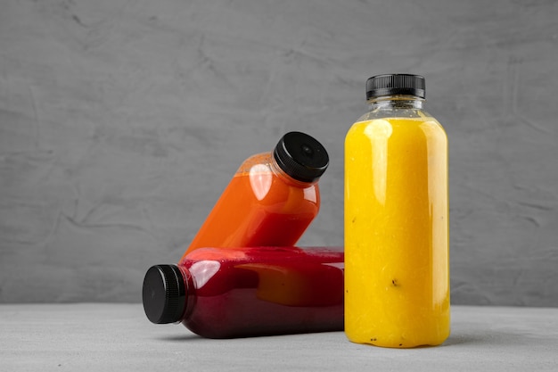 Photo trois bouteilles en plastique avec du jus fraîchement pressé sur gris