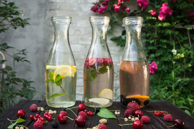 Trois bouteilles en verre avec boisson à la menthe et aux baies sont sur les planches sombres sur fond de mur de briques