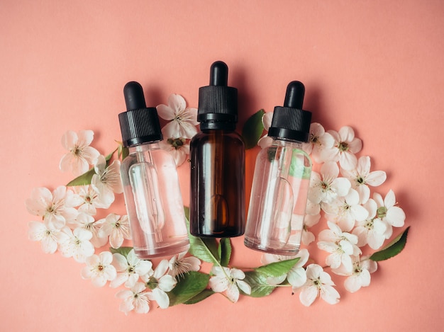 Trois bouteilles en verre d'huile, parfum sur une surface rose avec cerise en fleurs. Mise à plat, minimalisme.