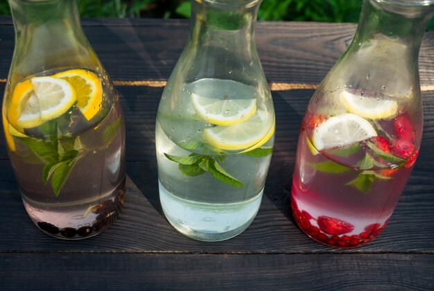 Trois bouteilles en verre avec un verre de menthe et de baies sur des planches sombres