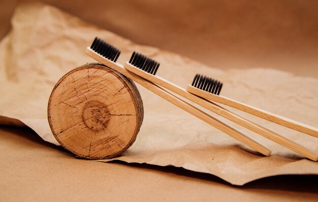 Trois brosses à dents en bambou naturel sont posées sur un morceau de bois, sur fond de papier kraft brun.