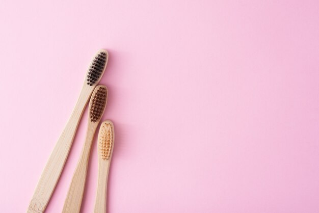 Trois brosses à dents en bois de bambou sur fond rose, vue de dessus. Concept de soins dentaires