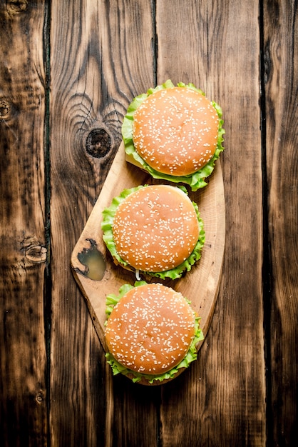 Trois burger fini avec de la viande et des légumes sur un support en bois. Sur fond de bois. Vue de dessus.