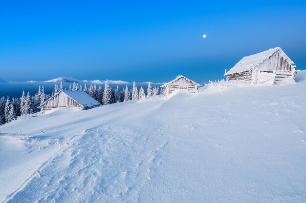 Trois cabanes en bois abandonnées dans les Carpates d'hiver au clair de lune