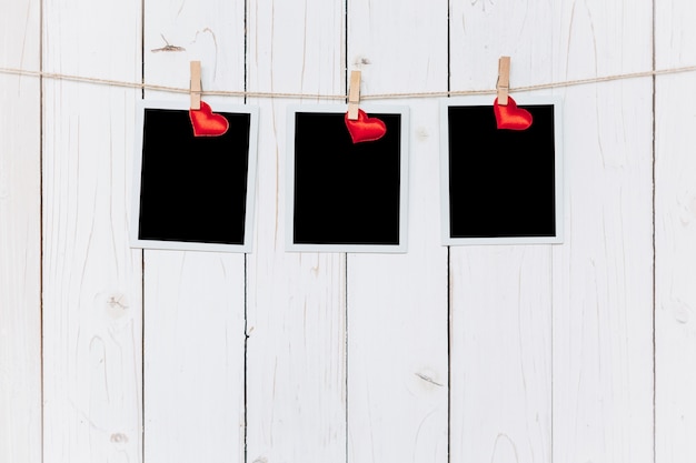 Photo trois cadres photo et coeur rouge suspendus sur fond blanc en bois avec de l'espace