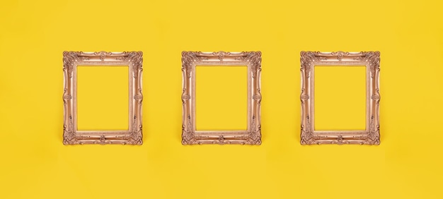 Trois cadres photo dorés ornés vides sur fond de mur jaune