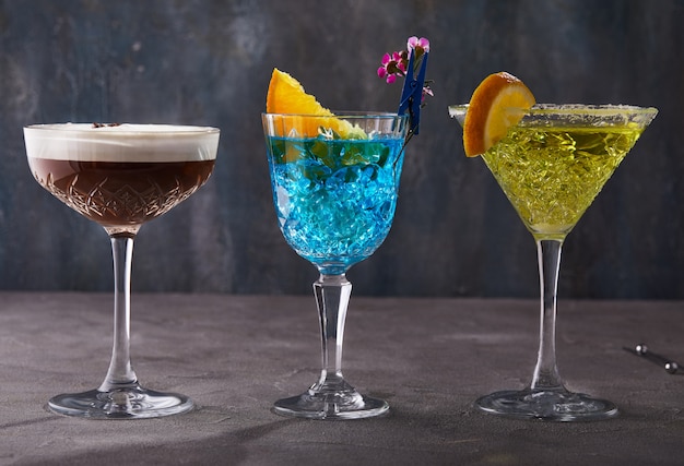 Trois cocktails Espresso martini, Curaçao bleu et Thea debout dans une rangée sur une table grise