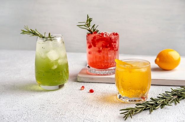 Trois cocktails d'été colorés dans des verres sur un tableau blanc.