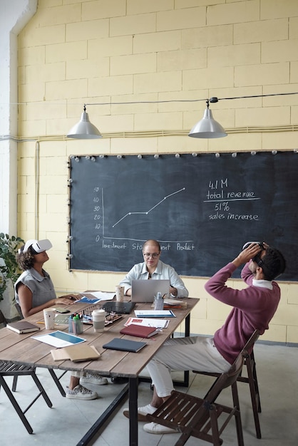 Photo trois collègues contemporains assis à table tandis que deux d'entre eux font une présentation virtuelle