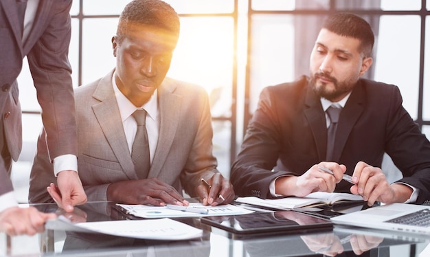 trois collègues d'un espace de travail moderne en train de parler et de sourire alors qu'ils sont assis à la table avec un ordinateur portable