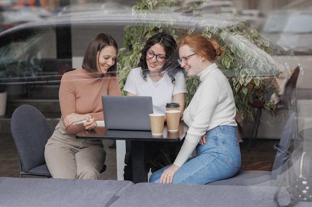 Trois collègues ou étudiantes travaillent sur un ordinateur portable et discutent d'un projet ou d'une dissertation créative trois amies en coworking travaillent en ligne sur un intranet