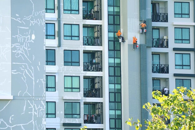 Trois cordistes peignant la façade d'un haut bâtiment moderne