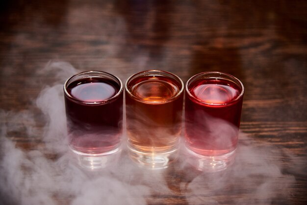 Photo trois coups d'alcool multicolores dans la fumée.