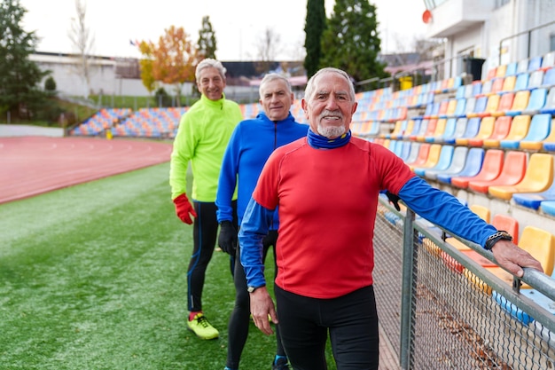 Photo trois coureurs âgés et joyeux se lient et sourient sur une piste colorée du stade.
