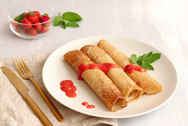 Trois crêpes recouvertes de sauce aux fraises et fraises sur une assiette