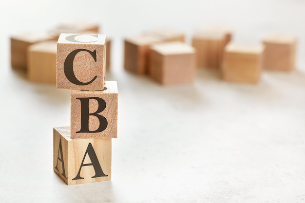 Trois cubes en bois avec des lettres CBA (signifie Cost Benefit Assessment), sur un tableau blanc, plus en arrière-plan, un espace pour le texte dans le coin inférieur droit