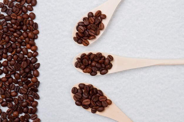 Trois cuillères à soupe en bois rustiques avec des grains de café. Tas de grain de café isolé sur une surface blanche