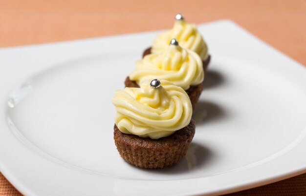 Trois cupcakes au chocolat avec des paillettes d'argent sur le dessus, sur une assiette blanche et une nappe en tissu