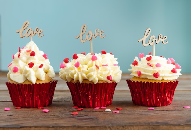 Trois cupcakes avec décoration de garniture rouge et un panneau en bois avec le mot LOVE sur un fond en bois. Copiez l'espace.