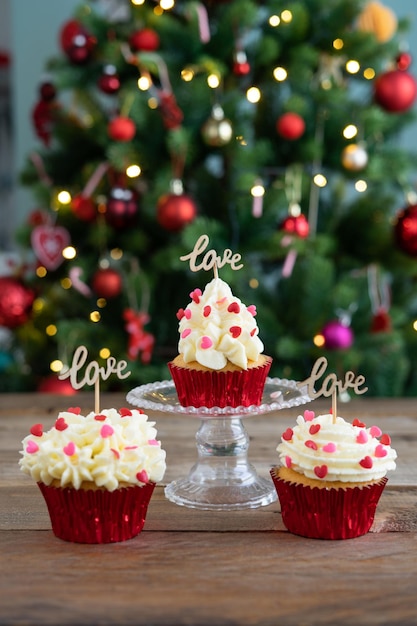 Trois cupcakes décorés sur fond de bois avec signe LOVE et sapin de Noël Copier l'espace photo verticale