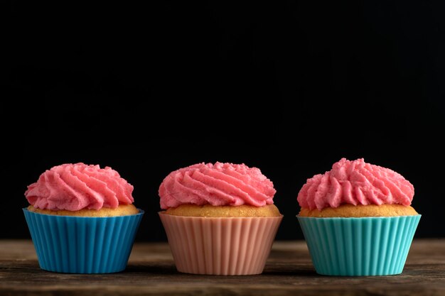 Trois cupcakes maison givrés avec un glaçage à la crème au beurre rose sur fond noir. Espace de copie.