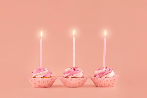 Trois cupcakes muffins d'anniversaire dans des emballages roses avec des bougies roses sur fond rose