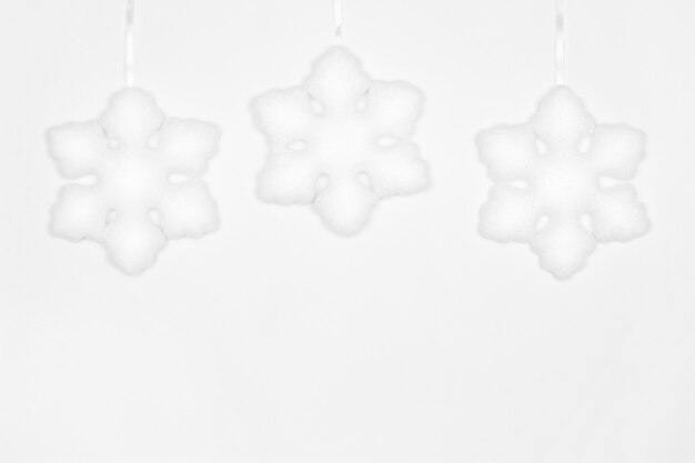 Photo trois décorations de flocon de neige blanches suspendues sur un mur blanc. espace de copie. fond d'hiver simple