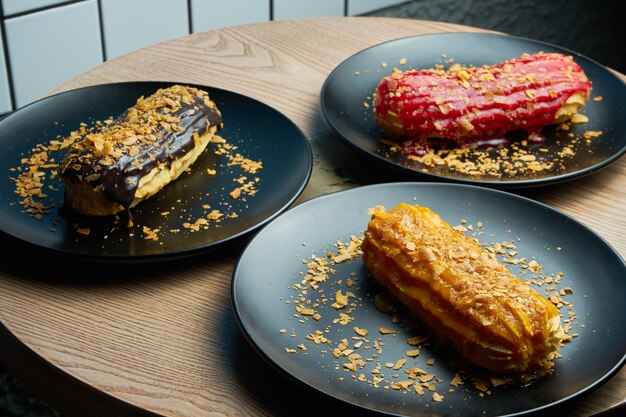 Trois éclairs appétissants et grands avec glaçage de dessus et crème de sapin à l'intérieur sur une plaque noire. Bonbons et dessert pour le café et le thé.