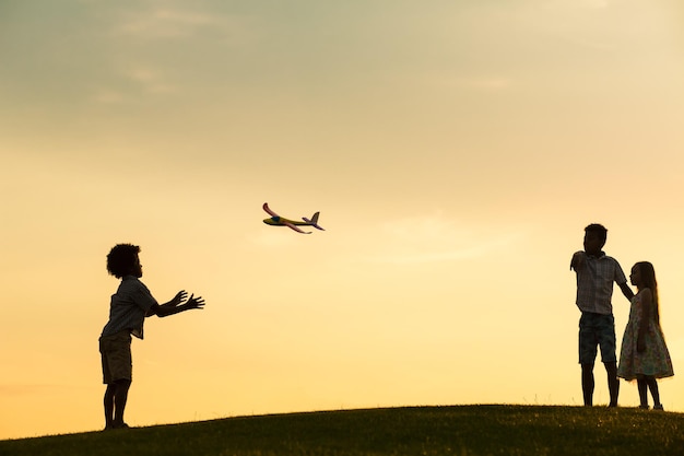 Trois enfants jouent avec un jouet d'avion au coucher du soleil.