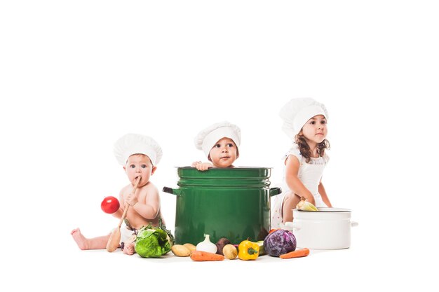 Trois enfants jouent avec des légumes. Petits chefs isolés sur blanc