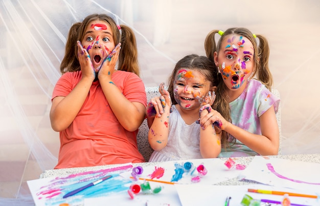 Trois enfants peignent avec des peintures. les filles sourient joyeusement et se moquent.