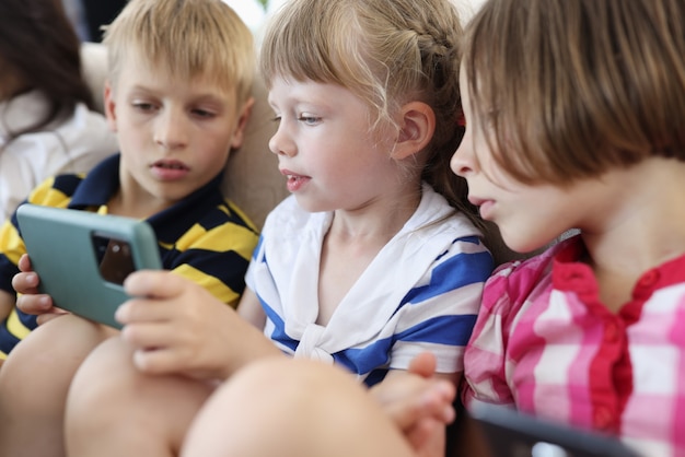 Trois enfants sont assis sur le canapé et regardent l'écran du smartphone.