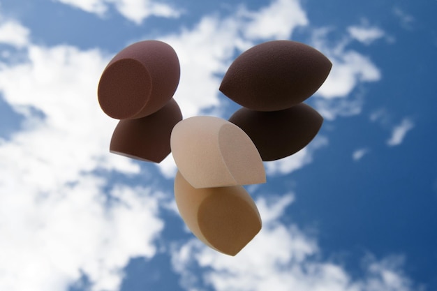 Trois éponges de formes et de couleurs différentes reposent sur le verre Des nuages blancs sont visibles dans le reflet Photo de mode Outils de maquillage