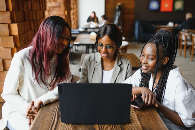 Trois étudiantes afro-américaines assises à la table d'un café étudiant pour un test ou faisant leurs devoirs ensemble, elles utilisent un ordinateur portable et une tablette numérique