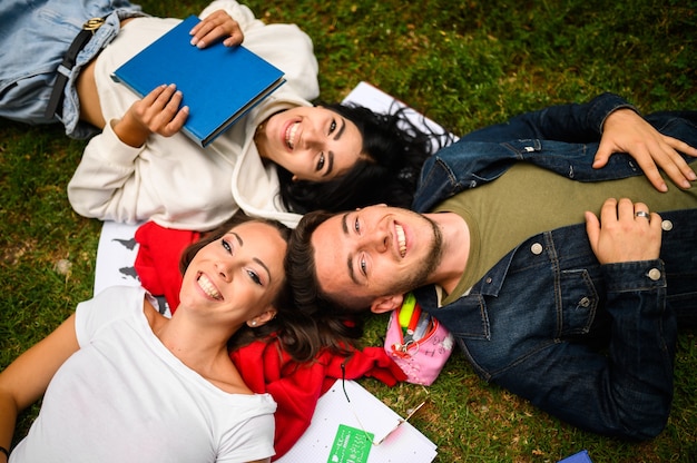 Trois étudiants allongés sur l'herbe et souriant