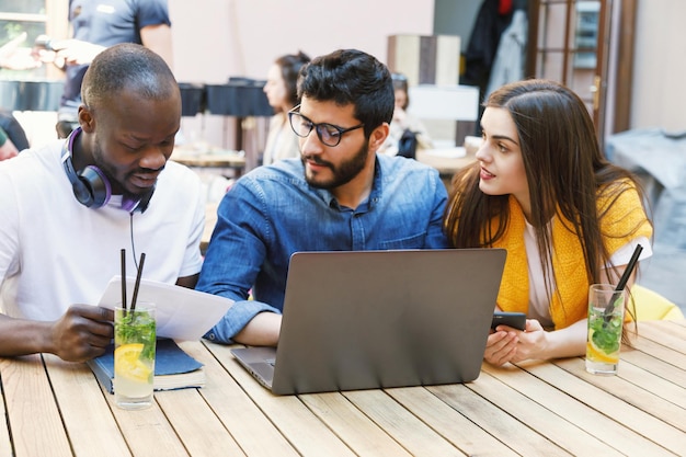 Trois étudiants intelligents multiculturels préparant des devoirs au café en plein air