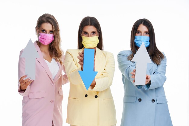 Trois femmes en costumes pastel posant avec des flèches sur fond blanc