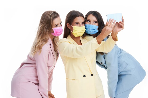 Trois femmes en costumes pastel posant avec des smartphones sur fond blanc