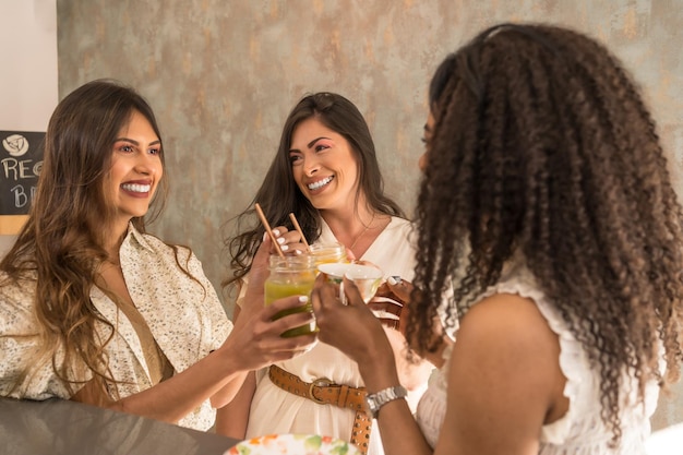 Trois femmes latines heureuses trinquant avec des jus de fruits dans une cafétéria