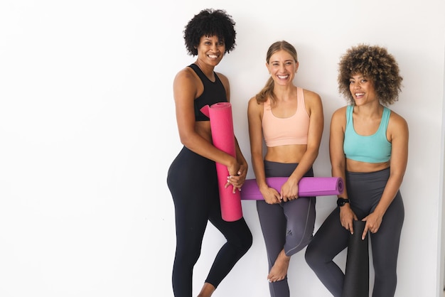 Trois femmes posent avec des tapis de yoga en souriant à la caméra