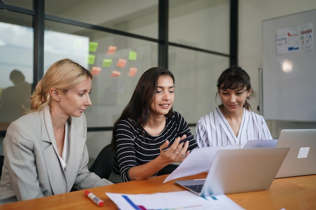 trois femmes sont assises à une table avec un ordinateur portable et l'une d'elles a un stylo dedans