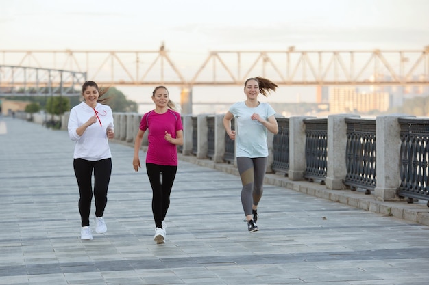 Trois femmes en tenue de sport courent le long de la berge de la rivière dans un parc en été.