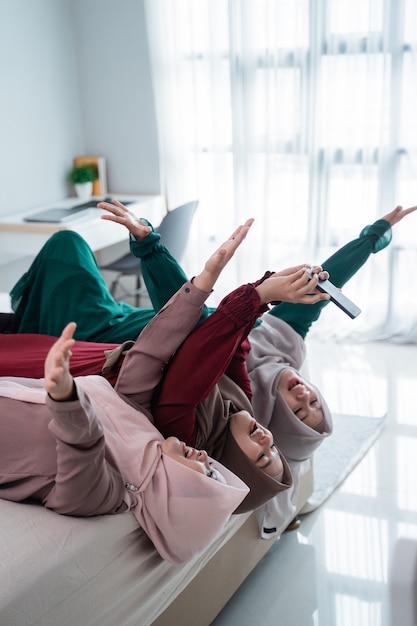 Trois femmes voilées se couchent et les mains levées sur le lit tout en prenant un selfie ensemble