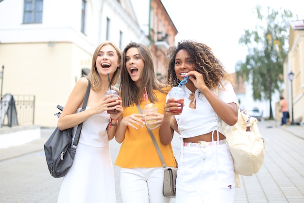 Trois filles branchées et branchées, des amis boivent un cocktail sur fond de ville urbaine.