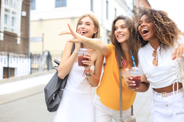 Trois filles branchées et branchées, des amis boivent un cocktail sur fond de ville urbaine.