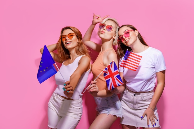 Trois filles dans des lunettes de vêtements d'été tenant des drapeaux de l'Union européenne, des États-Unis et de la Grande-Bretagne ...