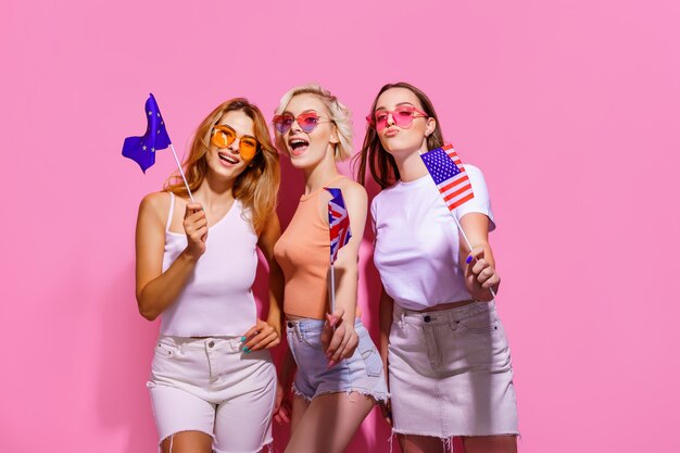 Trois filles dans des lunettes de vêtements d'été tenant des drapeaux de l'Union européenne, des États-Unis et de la Grande-Bretagne ...